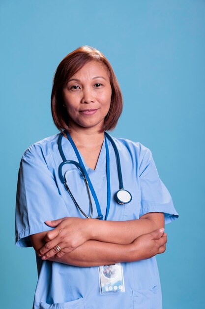 Sorridente medico infermiere che indossa stetoscopio e uniforme blu durante la consultazione medica che lavora nel settore sanitario. Assistente asiatico sorridere alla telecamera in piedi in studio con sfondo blu