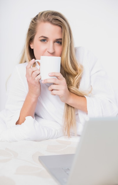 Sorridente modello grazioso bere caffè sdraiato sul letto accogliente