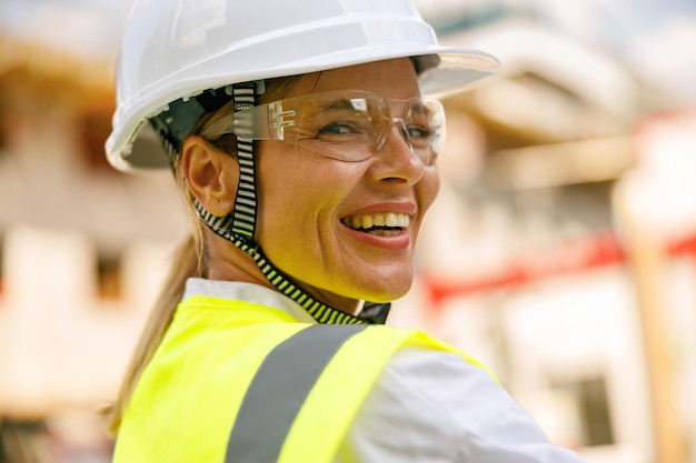 Sorridente operaio edile femminile in casco protettivo in piedi contro sullo sfondo della costruzione