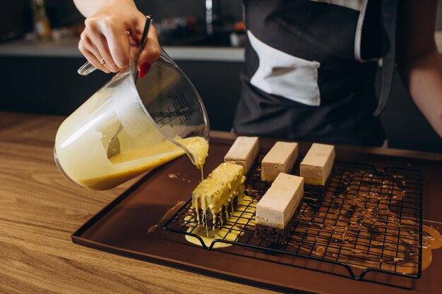 Sorridente pasticcere che versa gommage al cioccolato liquido sulla torta di biscotti in forma di metallo che lavora al servizio di catering ristorante Donna chef in uniforme al processo di assemblaggio del dessert di mousse