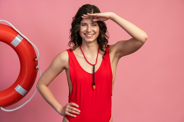 Sorridente, positiva, giovane ragazza in un sexy costume da bagno rosso si mise la mano sulla fronte, cercando qualcuno. Bagnino su sfondo rosa