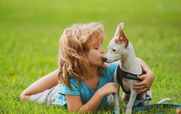 Sorridente proprietario bambino sdraiato sul prato con un cucciolo felice alla pecorina che gioca con il cane sul prato