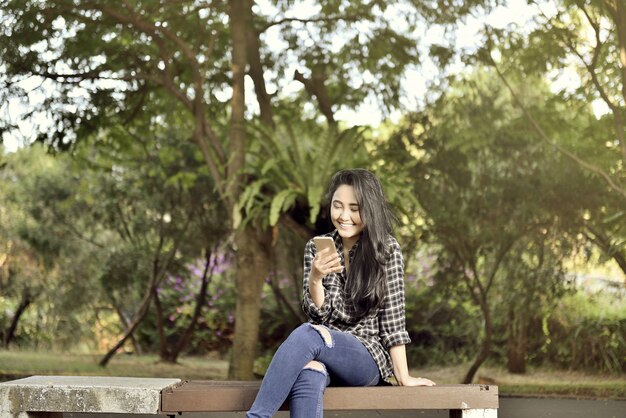 Sorridente ragazza asiatica con seduta di telefonia mobile