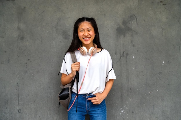 Sorridente ragazza asiatica studentessa delle scuole superiori in piedi all'aperto guardando la fotocamera Concetto di istruzione e stile di vita