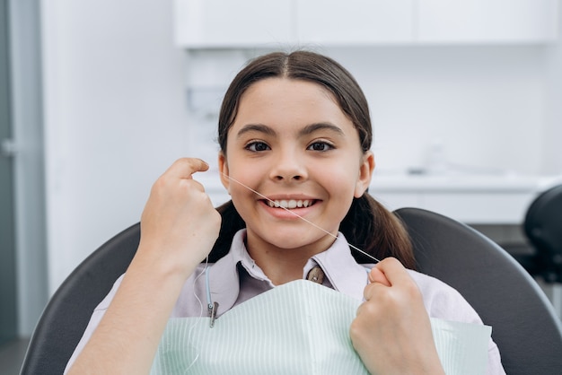 Sorridente, ragazza attraente che tiene il filo per i denti. Ragazza dal dentista, cure dentistiche