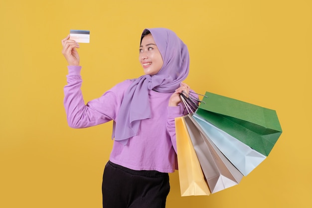 Sorridente ragazza carina felice utilizzando la carta di credito per sprecare soldi nel centro commerciale, tenendo le borse della spesa, comprare regali o regali, concediti la giornata