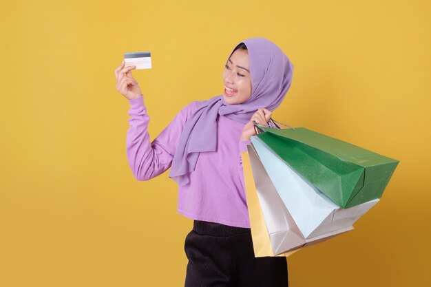 Sorridente ragazza carina felice utilizzando la carta di credito per sprecare soldi nel centro commerciale, tenendo le borse della spesa, comprare regali o regali, concediti la giornata