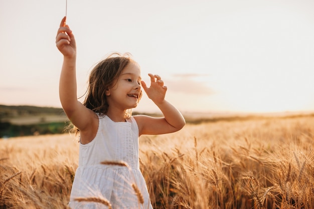 Sorridente ragazza caucasica vestita in abito bianco sta camminando in un campo di grano con un sorriso allegro sui salti