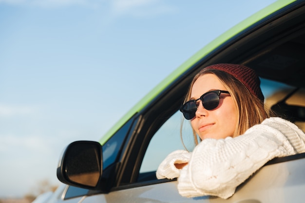 Sorridente ragazza giovane alla guida di un'auto durante il tramonto, guardando la finestra