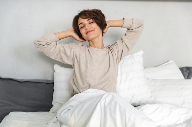 Sorridente ragazza giovane rilassante a letto la mattina, allungando le mani