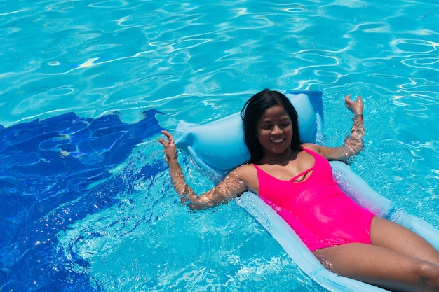 Sorridente ragazza in bikini divertirsi sul gonfiabile in piscina. Donna che prende il sole a una festa tropicale. Donna di colore carina sotto il sole.