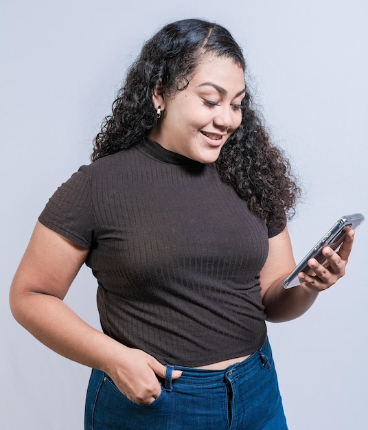 Sorridente ragazza latina utilizzando il cellulare isolato Allegra giovane donna con i capelli ricci SMS sul cellulare isolato