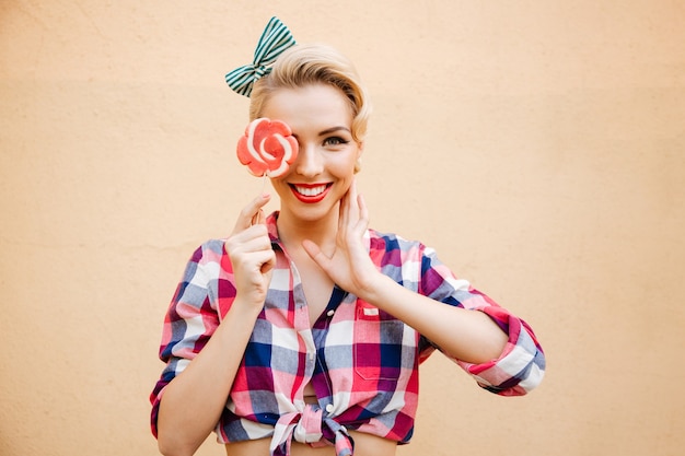 Sorridente ragazza Pin-up in posa all'aperto, si copre gli occhi con lecca-lecca