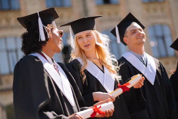 Sorridente ragazzo e ragazza che indossano abiti da laurea e berretti maestri che parlano durante la laurea