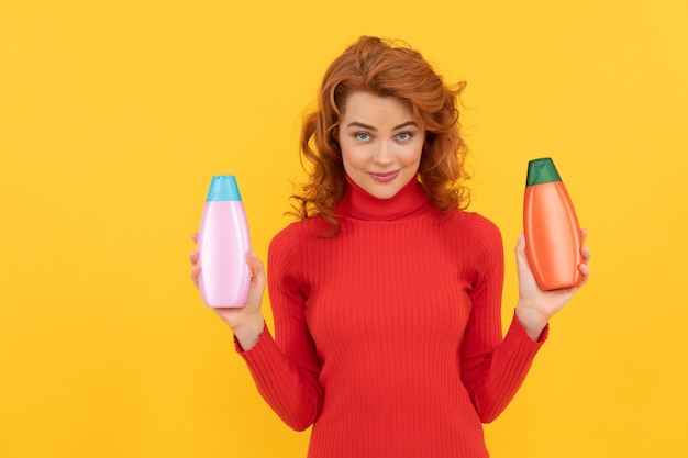 Sorridente signora rossa capelli tinti ricci scegliendo il prodotto per la cura del corpo della bottiglia di shampoo, scelta.