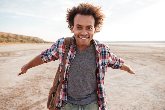 Sorridente simpatico giovane africano con le braccia aperte aperte in spiaggia