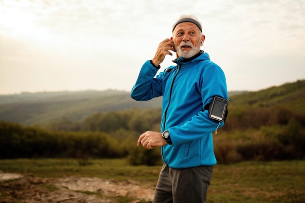 Sorridente sportivo senior che ascolta musica mentre si prepara per correre in natura Spazio di copia