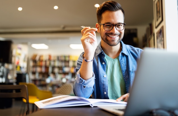 Sorridente studente maschio che lavora e studia in una biblioteca