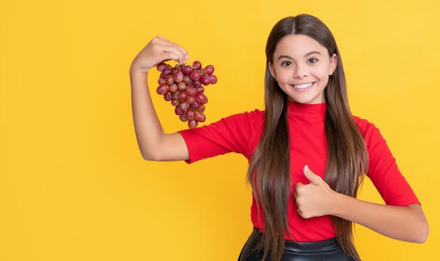 Sorridente teen kid tenere grappolo d'uva su sfondo giallo