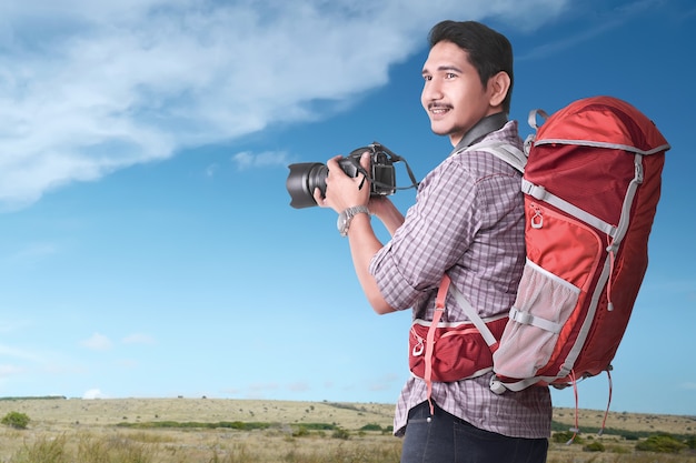 Sorridente turista asiatico con zaino e macchina fotografica