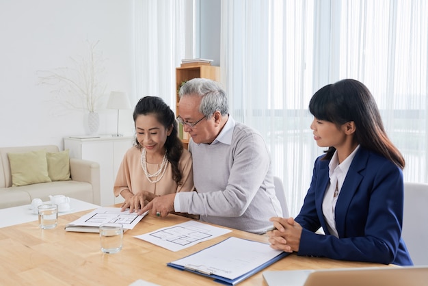 Sorridente uomo anziano e donna che si incontrano con un agente immobiliare e guardano e costruiscono piani quando...