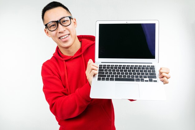 Sorridente uomo attraente brunetta dimostra uno schermo di computer portatile vuoto con mockup nelle sue mani su uno sfondo bianco studio.