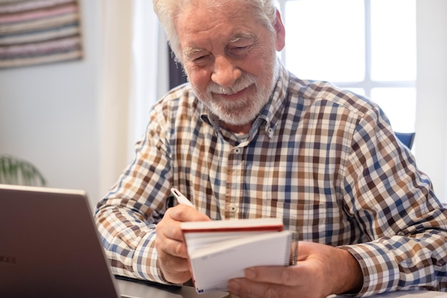 Sorridente uomo barbuto maturo seduto al tavolo con laptop e libri seguendo il corso online