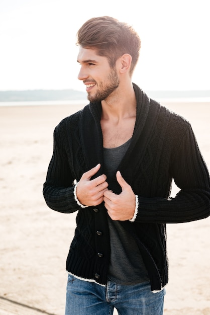 Sorridente uomo casual che attraversa la spiaggia al sole del mattino