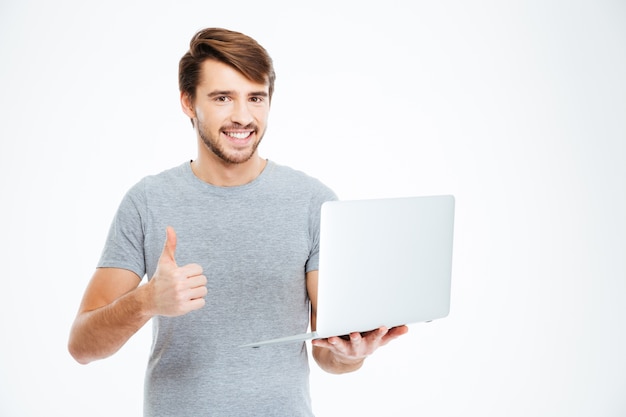 Sorridente uomo casual tenendo il computer portatile e mostrando il pollice in alto isolato su uno sfondo bianco white