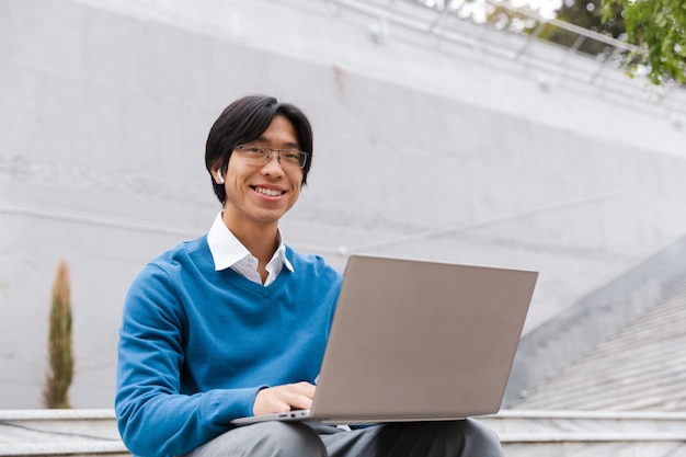 Sorridente uomo d'affari asiatico utilizzando il computer portatile all'aperto