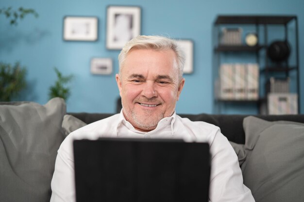 Sorridente uomo di mezza età rilassante tenendo tablet digitale lettura e libro sedersi sul divano a casa