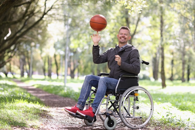 Sorridente uomo disabile fa roteare la palla da basket sul dito mentre è seduto su una sedia a rotelle nel parco