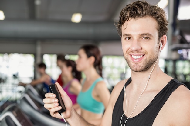 Sorridente uomo muscoloso sul tapis roulant, ascoltando musica in palestra