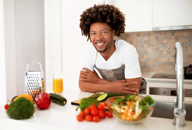 Sorridente uomo nero in posa durante la preparazione di una sana cena in cucina