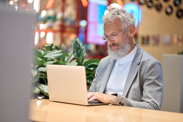 Sorridente vecchio uomo d'affari senior utilizzando il computer portatile lavorando fino a tardi sul computer