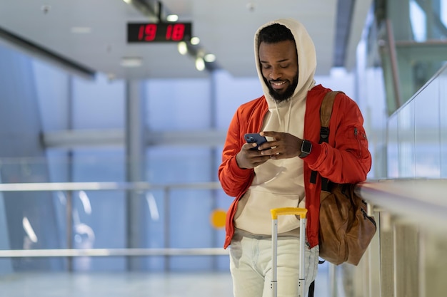 Sorridente viaggiatore afroamericano in chat sui social media in attesa di atterraggio a bordo in aeroporto