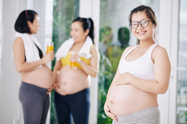 Sorridenti giovane donna incinta con gli occhiali toccando la pancia