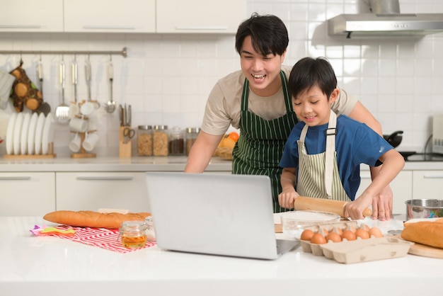 Sorridenti giovani asiatici padre e figlio che effettuano una videochiamata alla madre si divertono a cucinare in cucina