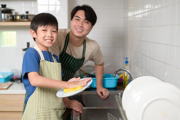 Sorridenti giovani asiatici padre e figlio lavare i piatti in cucina a casa