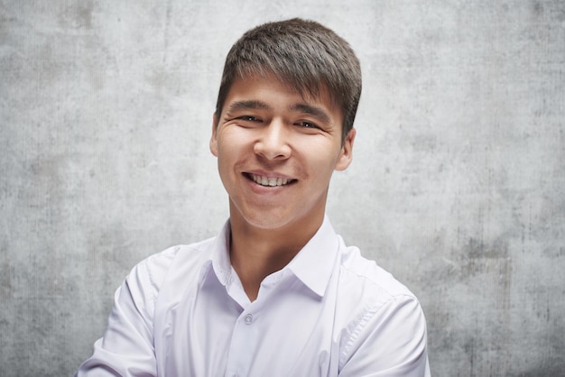 Sorridere a trentadue denti dell'uomo d'affari asiatico. Ritratto di un giovane studente kazako attraente in una camicia bianca in studio