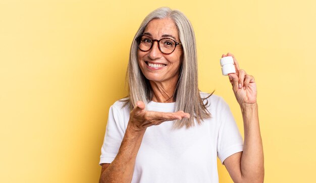 Sorridere allegramente, sentirsi felici e mostrare un concetto nello spazio della copia con il palmo della mano e tenere una bottiglia di pillole