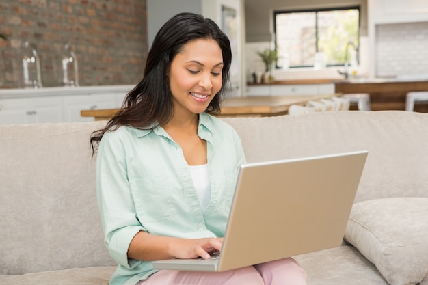 Sorridere castana facendo uso del computer portatile sul sofà