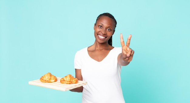 Sorridere e sembrare amichevole, mostrando il numero due e tenendo in mano un vassoio di croissant