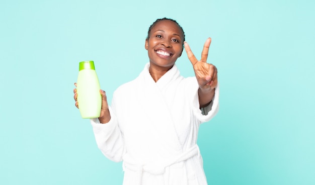 Sorridere e sembrare felice, gesticolare vittoria o pace indossando l'accappatoio e tenendo in mano uno shampoo