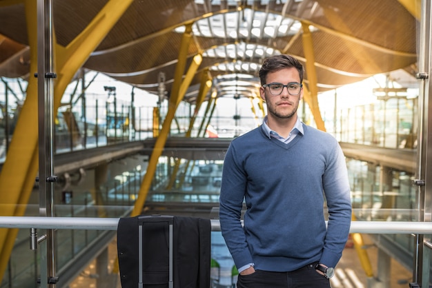 Sorridere felice del giovane uomo bello all'aeroporto che aspetta il suo volo con bagagli