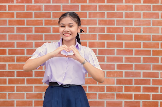 Sorridere felice del ritratto di gesto del segno del cuore di amore della mano dello studente asiatico.