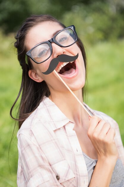 Sorridere grazioso del brunette alla macchina fotografica con i baffi falsi