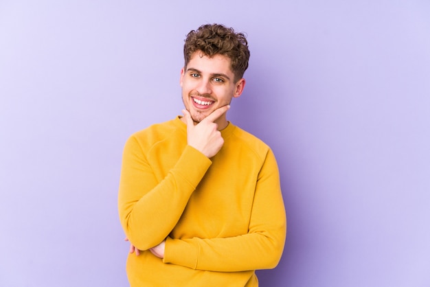 Sorridere isolato felice e sicuro, mento commovente dell'uomo caucasico dei giovani capelli ricci biondi con la mano.