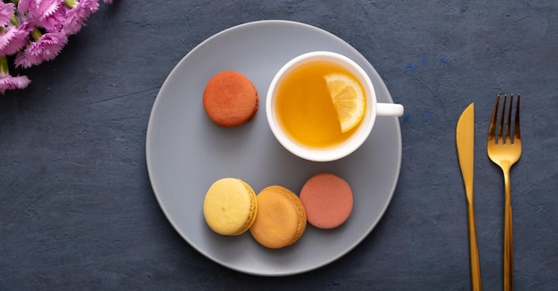 Sorridi con amaretti e tazza di tè su un piatto su un tavolo di pietra scuro con fiori Bellissimo delizioso dessert