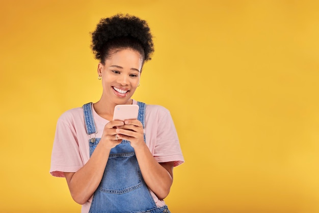 Sorridi digitando e donna con il telefono in studio che invia messaggi di testo o post sui social media con mockup su sfondo giallo Chat di rete online e modello felice con l'app mobile per cellulare che legge meme o e-mail